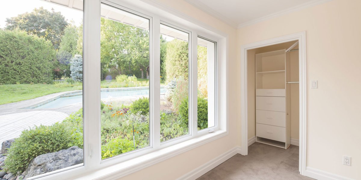 Room with large windows overlooking a garden and pool, with an open closet on the right.