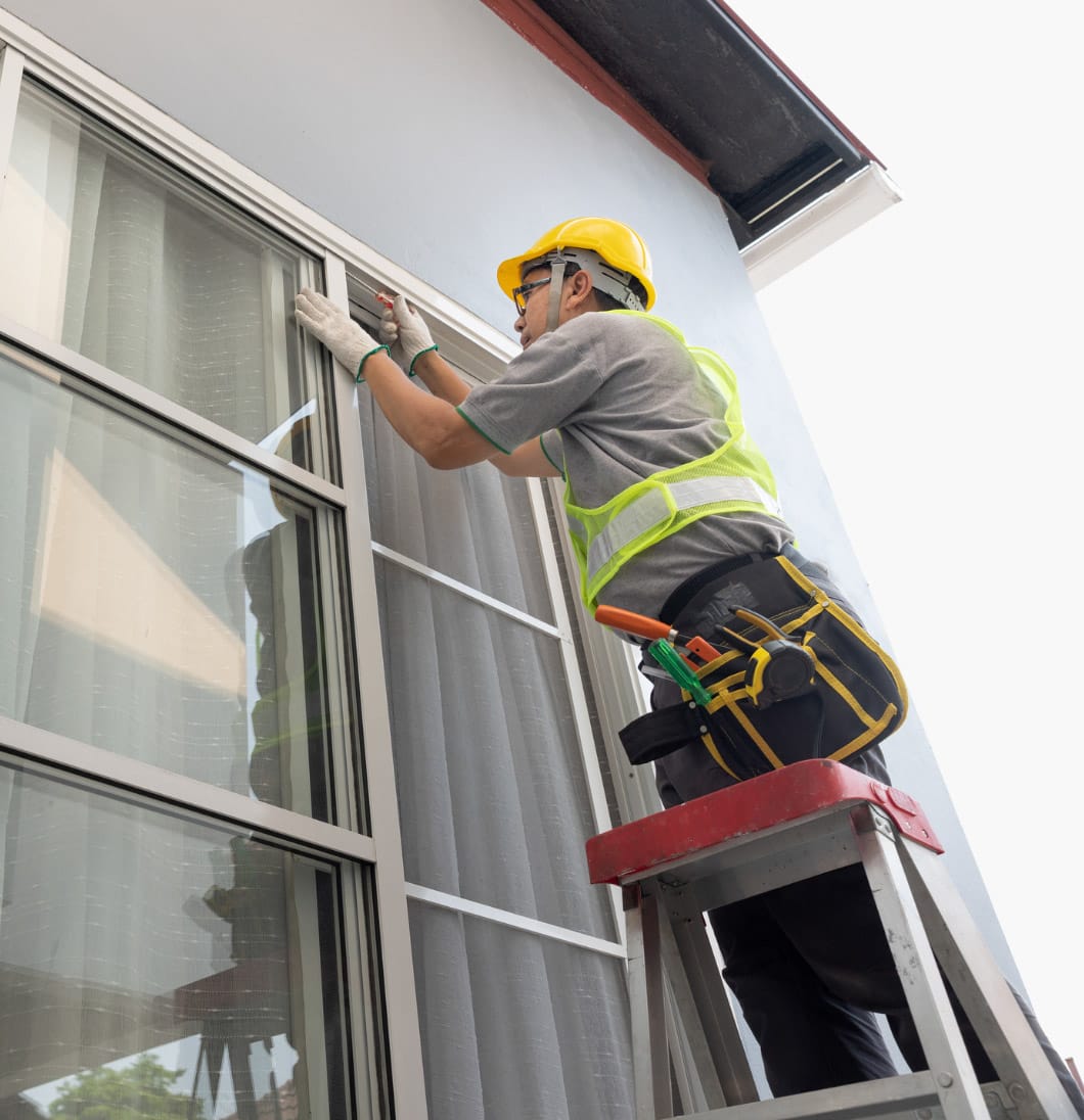 sliding-installation-img Worker in a yellow helmet and vest repairs a window using tools on a ladder.
